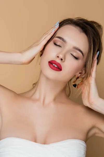 charming woman with closed eyes and naked shoulders touching hair isolated on beige