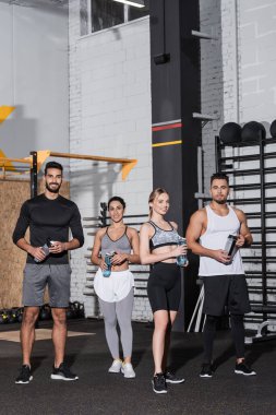 Spor salonunda spor şişeleri tutan pozitif çok ırklı insanlar. 
