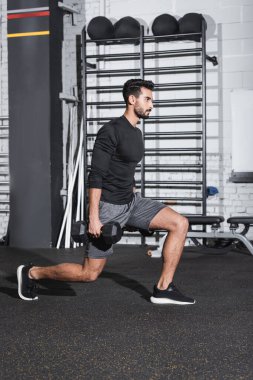 Spor salonunda halterlerle atlama yapan Arap sporcunun yan görüntüsü 