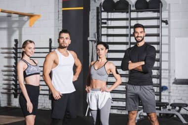 Spor giyim sektöründe gülümseyen çok ırklı insanlar spor merkezindeki kameralara bakıyor. 