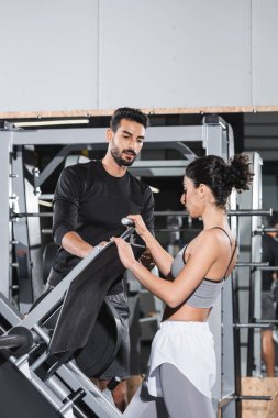 Orta Doğulu sporcu kadın spor salonunda bacak pres makinesi ve müslüman antrenörünün yanında duruyor. 