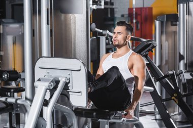 Spor giyiminde sporcu spor salonundaki spor malzemelerinin yanında bacak pres makinesi eğitimi alıyor. 