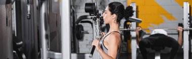 Young middle east woman training on lat pulldown machine in sports center, banner  clipart