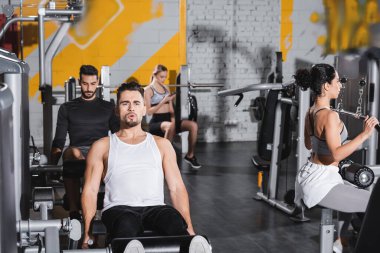 Spor merkezinde ırklar arası insanların yanında bacak kıvırma makinesinde sporcu eğitimi 