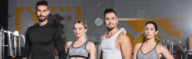 Spor giyim sektöründe çok ırklı gençler spor salonunda kameraya bakıyor. 
