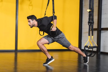 Spor salonundaki askılarla çalışan müslüman sporcunun yan görüntüsü 