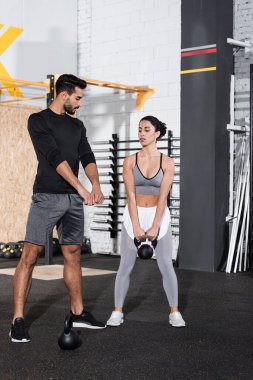 Orta Doğu sporcusunun yanında spor salonunda kettlebell ile antrenman yapan Arap antrenör. 