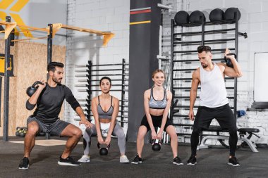 Gülümseyen çok ırklı insanlar spor merkezinde çan sesleri ile antrenman yapıyorlar. 