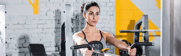 Young middle east sportswoman training on ab crunch machine in gym, banner 