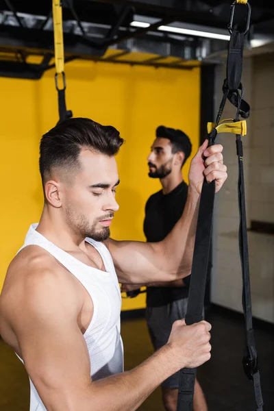 Young Man Holding Suspension Straps Blurred Arabian Friend Gym — Stock Photo, Image