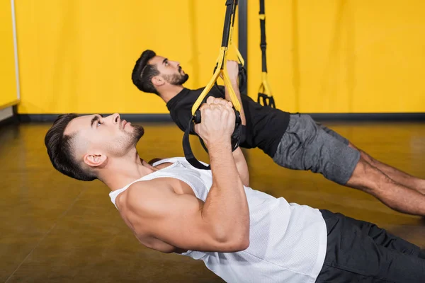 Side View Athletic Sportsman Pulling Suspension Straps Blurred Arabian Friend — Stock Photo, Image