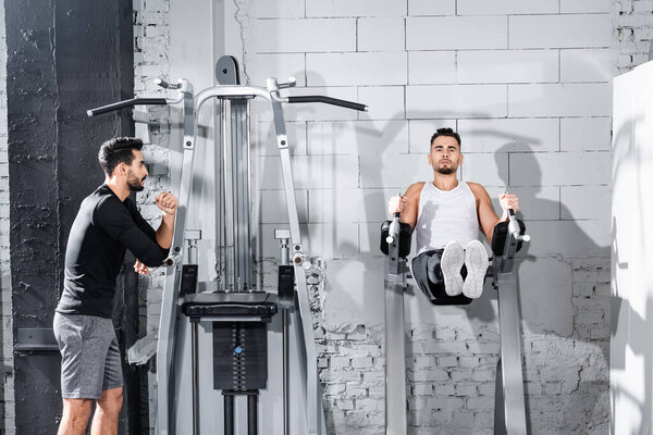 Sportsman training on parallel bar near arabian trainer in gym 