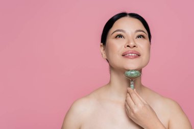 Çıplak omuzlu Asyalı bir kadın. Yüzüne masaj yapıyor. Yeşim takla atıyor. 