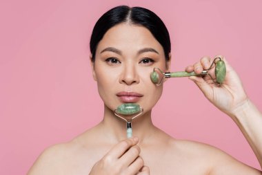 Yüzüne masaj yapan Asyalı kadın. Pembeye izole edilmiş yeşil bigudileri var. 