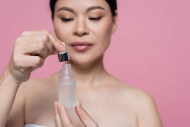 Bulanık Asyalı kadının elinde bir şişe serum. Pembe üzerine izole edilmiş. 