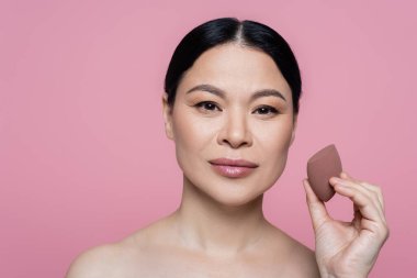 Çıplak omuzlu Asyalı bir kadın güzellik blenderi tutuyor. Pembe üzerine izole edilmiş. 