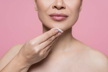 Çıplak omuzlu, çene temizleyen, pamuklu yastıklı pembe elbiseli kadın görüntüsü. 