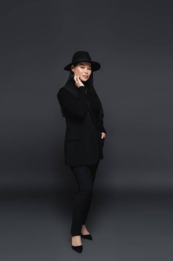 Fötr şapkalı Asyalı kadın koyu gri arka planda poz veriyor. 