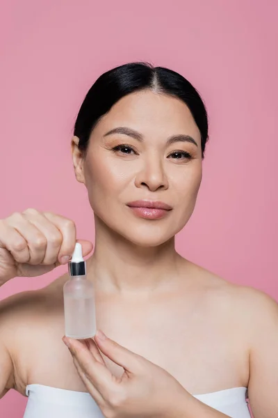 Asian woman in top holding serum isolated on pink