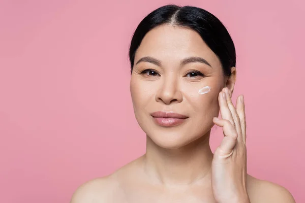 Mulher Asiática Aplicando Creme Cosmético Olhando Para Câmera Isolada Rosa — Fotografia de Stock