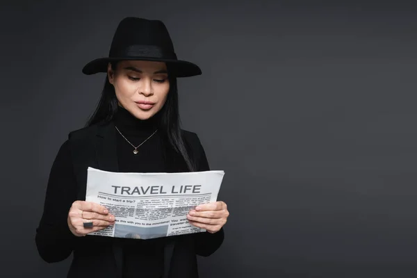 Stylish asian woman reading newspaper isolated on dark grey