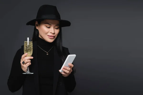 Glimlachende Aziatische Vrouw Fedora Hoed Met Smartphone Glas Champagne Geïsoleerd — Stockfoto