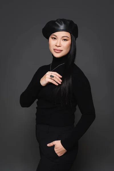 Stylish asian woman in beret posing isolated on dark grey