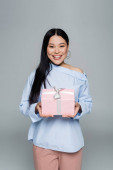 Radostná asijská žena drží dárek izolované na šedé 