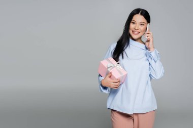 Neşeli Asyalı kadın Griler 'de izole edilmiş akıllı telefonla konuşuyor. 