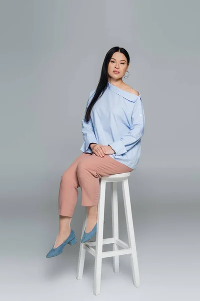 亚洲模特坐在灰色背景的椅子上看着相机 — 图库照片
