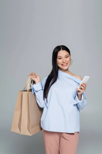 Sorrindo Asiático Mulher Segurando Smartphone Compras Sacos Isolados Cinza — Fotografia de Stock