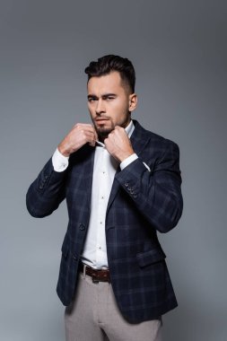 Kareli ceketli sakallı işadamı gri yakalı beyaz yakalıyı düzeltiyor.