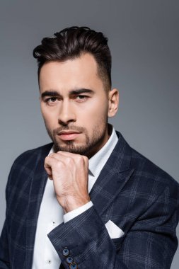 Ekose ceketli sakallı işadamı gri renkli kameraya bakıyor. 