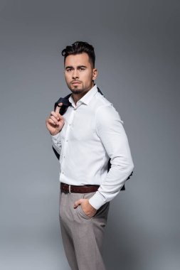 Genç sakallı iş adamı spor ceketini tutuyor ve gri üzerinde el ele duruyor.