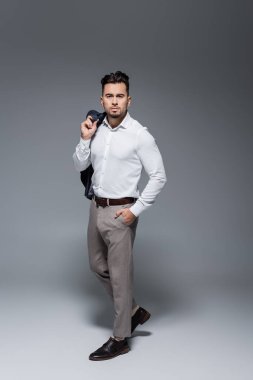 Uzun boylu, sakallı bir iş adamı spor ceketini tutuyor ve gri ceketin cebinde duruyor.