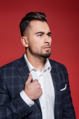 Beyaz gömlekli ve kareli ceketli sakallı işadamı kırmızıya bakıyor.