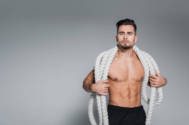Üstsüz sporcu ağır savaş iplerini gri omuzlarında tutuyor.