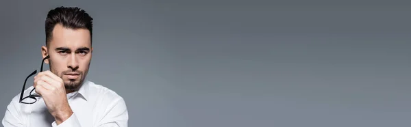 Бородатый Бизнесмен Белой Рубашке Держащий Очки Смотрящий Камеру Изолированную Сером — стоковое фото