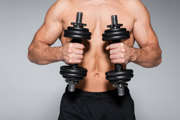partial view of shirtless and muscular sportsman working out with dumbbells isolated on grey
