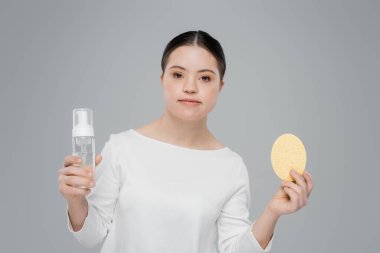 Woman with down syndrome holding cleansing foam and sponge isolated on grey  clipart