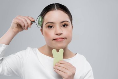Woman with down syndrome holding jade roller and stone isolated on grey  clipart
