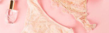 Pembe arka planda, parfümün yanındaki şeftali rengi iç çamaşırı manzarası. 