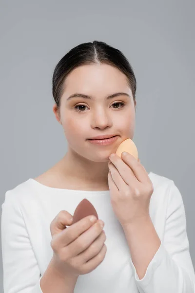 Woman with down syndrome holding beauty blenders isolated on grey