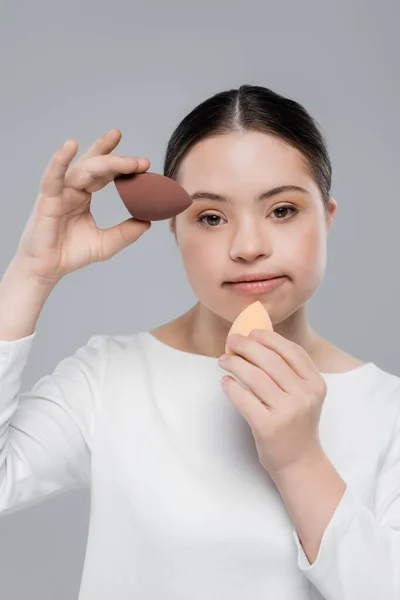 Woman with down syndrome holding beauty blenders isolated on grey