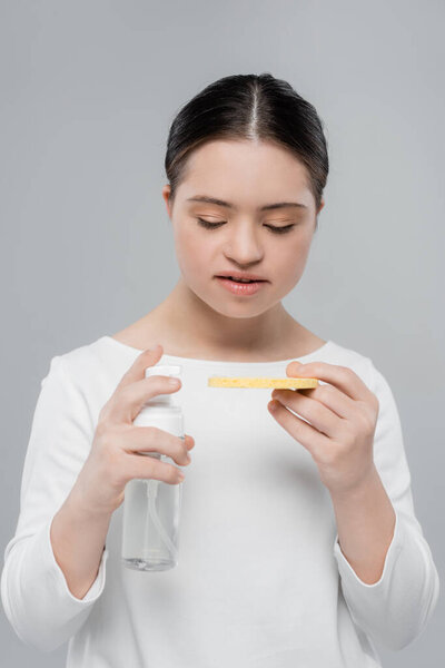 Woman with down syndrome holding sponge and cleansing foam isolated on grey 