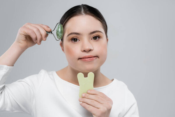 Woman with down syndrome holding jade roller and stone isolated on grey 