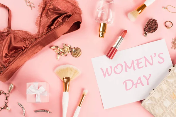 在粉红背景的化妆品刷子 胸罩和礼物旁边贴上女用字母的卡片的顶部视图 — 图库照片