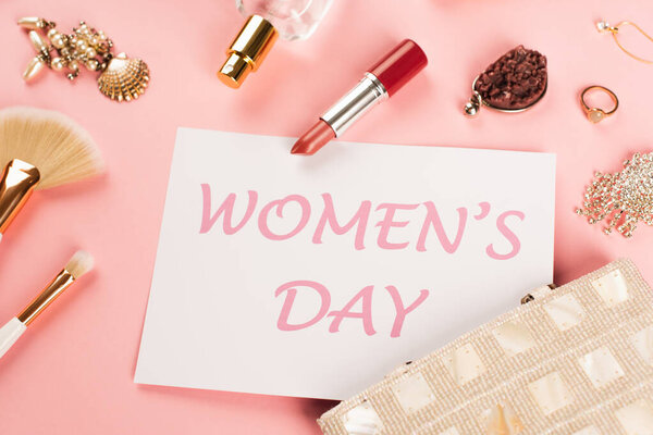 Top view of card with womens day lettering near perfume and accessories on pink background 