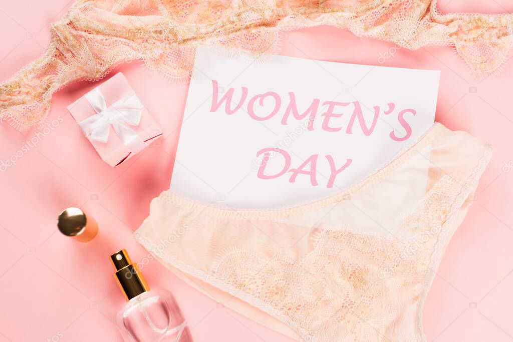 Top view of peach lace lingerie near perfume, gift and card with womens day lettering on pink background 