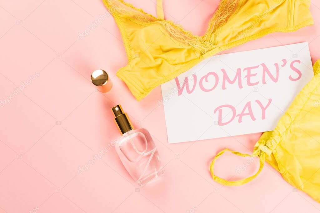 Top view of card with womens day lettering near perfume and bra on pink background 